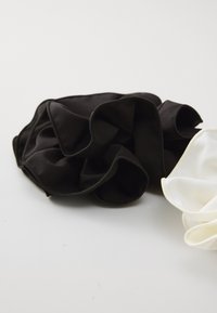 Twee scrunchies worden getoond: een zwarte en een witte. De zwarte scrunchie heeft een gladde textuur en een gerimpeld ontwerp; de witte scrunchie heeft een vergelijkbare structuur.