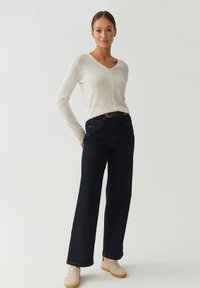 Hvid langærmet sweater med v-hals, parret med mørkeblå højtaljede jeans og beige sneakers, der har et struktureret stof og en afslappet pasform.