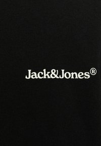 Sort t-shirt med ribbet tekstur, der har "Jack&Jones" logoet i hvidt, placeret centralt over taljen. Registreret varemærkesymbol inkluderet.