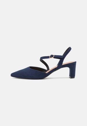 Chaussure slingback en daim bleu marine à petit talon, bout pointu et fine bride de cheville avec une petite boucle ronde.