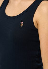 Mörkblå randig linne med en liten broderad logotyp på vänster sida. Tyget är mjukt med en figurnära design och breda axelremmar.