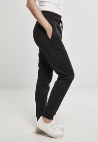 Schwarze Jogginghosen aus weichem Material mit Kordelzugbund, Seitentaschen und elastischen Knöcheln, kombiniert mit weißen Sneakers.
