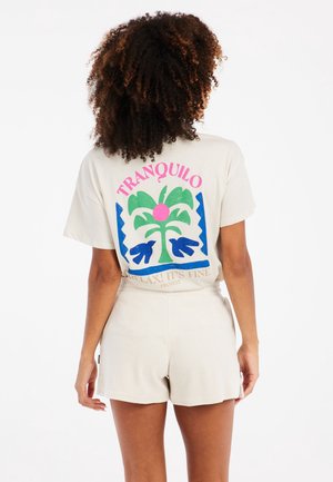 Crème t-shirt met een kleurrijke palmgrafiek met roze en blauwe accenten, gecombineerd met lichtbeige shorts in een zachte textuur.