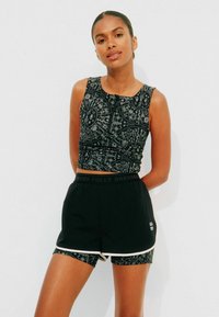 Zwart crop top met ingewikkelde zilveren patronen, gecombineerd met zwarte shorts met een merkband en contrasterende bies.
