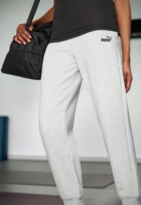 Pantalons de survêtement en coton gris avec taille élastique et poignets côtelés, arborant le logo noir "PUMA"; associés à un sac de sport en maille noir.