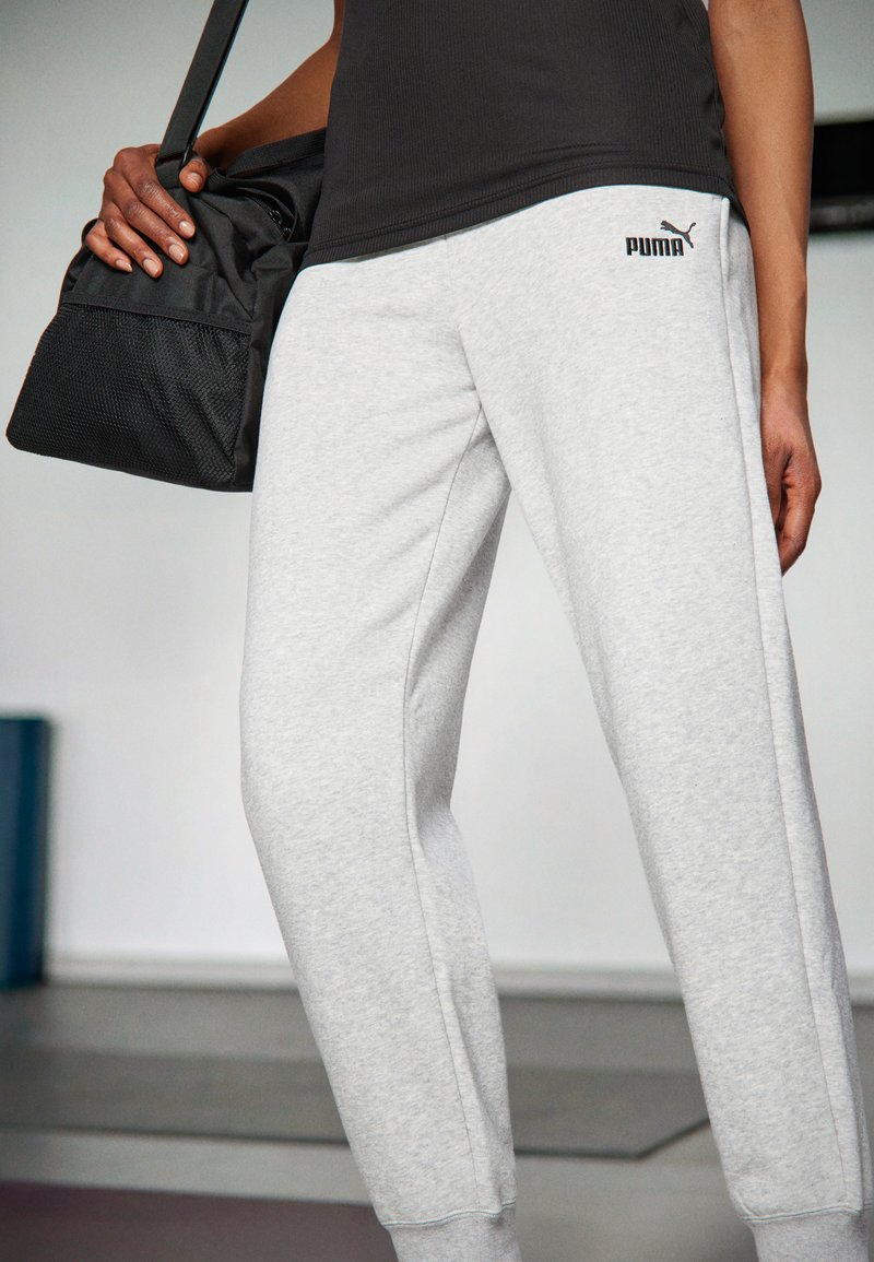 Pantalons de survêtement en coton gris avec taille élastique et poignets côtelés, arborant le logo noir "PUMA"; associés à un sac de sport en maille noir.