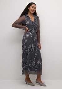 Duga, mornarsko plava haljina s V-izrezom, prozirnim dugim rukavima i cvjetnim sequin ukrasima. Tkanina je teksturirana s vertikalnim prugama.