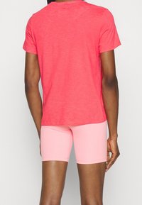 Camiseta coral de manga corta con un corte holgado, combinada con pantalones cortos deportivos rosa claro, mostrando una tela suave y un diseño sencillo.