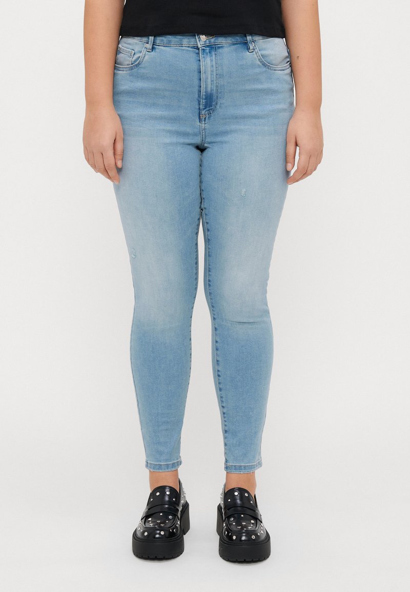 Light blue skinny jeans with a slightly faded finish, featuring a button closure and five-pocket design, paired with chunky black platform shoes.