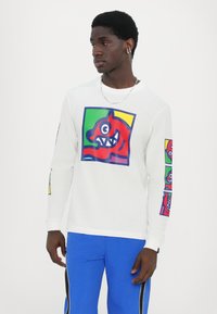 Langarm-weißes T-Shirt mit bunten Monstergrafiken auf der Vorderseite und den Ärmeln. Baumwollstoff mit normaler Passform und Rundhalsausschnitt.