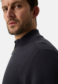 Dunkelblauer, gestrickter Pullover mit hohem Kragen, einem Reißverschluss vorne und strukturierten Mustern entlang der Schultern.