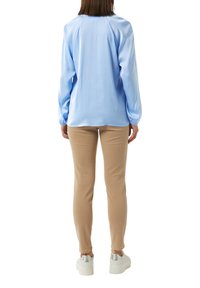 Himmelblaues Satin-Hemd mit langen Ärmeln und gerafften Manschetten, kombiniert mit engen beigen Hosen und weißen Plateausneakern mit silbernen Akzenten.