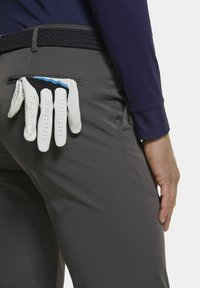 Grijze broek met een gevlochten zwarte riem. Witte golfhandschoenen met blauwe en zwarte accenten die uit de achterzak komen. Glad stofoppervlak.