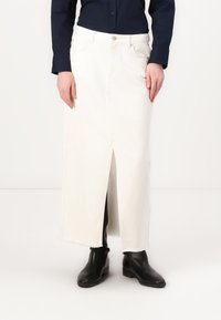 Hvit denim maxi-skjørt med slisse foran, frynset kant og sidelommer. Brukt med svarte ankelboots og en marineblå skjorte med knapper.