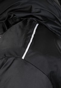 Close-up of black textured fabric with a white reflective strip, showing detailed stitching and material texture.