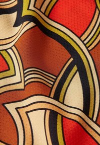 Patterned fabric featuring bold, curvilinear designs in red, orange, cream, and black, with dotted texture and prominent graphic lines.