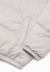 Light gray puffer jacket section featuring a smooth texture, elastic cuffs, and a side pocket with a concealed opening.