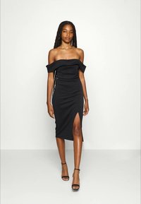 Fekete, váll nélküli ruha, testhez simuló fazonnal, térd alatt végződik, és oldalsó hasítékkal rendelkezik. Sima anyag, elegáns textúrával.