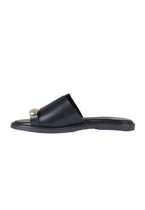Sandalo scivolo in pelle nera con cinturino largo, anello per l'alluce e bottone decorativo rotondo dorato su sfondo bianco.