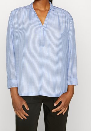 Niebiesko-biała koszula w pionowe paski z długim rękawem i kołnierzem w serek, noszona z czarnymi spodniami.