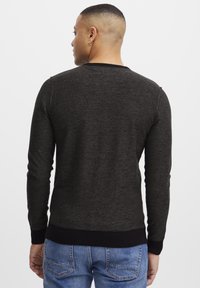 Mørkegrå strikket genser med lange ermer, ribbestrikkede mansjetter og kant, samt rund hals, brukt med blå jeans. Glatt tekstur, avslappet passform.