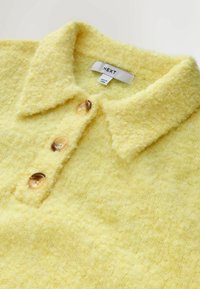 Żółty sweter polo o fakturowanej powierzchni z miękkim wykończeniem, z kołnierzykiem i trzema brązowymi guzikami. Metka mówi "NEXT."