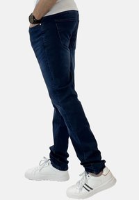 Jeans blu scuro con vestibilità slim, caratterizzati da un design a cinque tasche e dettagli di cucitura delicati, abbinati a sneaker bianche.