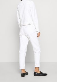 Chaqueta de mezclilla blanca con un corte cropped, que cuenta con dos botones en la parte trasera. Combinada con jeans blancos de tiro alto y mocasines negros. Textura suave.