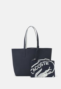 Sac cabas bleu marine à texture lisse, avec deux longues poignées et une pochette noire amovible arborant un logo blanc et un design de crocodile.