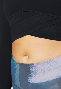 Top aderente nero con texture a costine, abbinato a leggings multicolori con motivi astratti blu e viola. Visibilità della zona centrale del corpo.