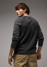 Grå stickad tröja med ribbad textur och åtsittande ärmar, med subtila detaljer längs axlarna, tillsammans med khakifärgade byxor.