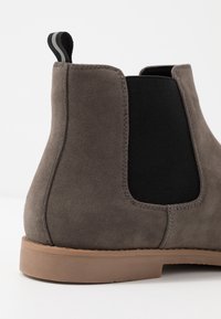 Szare zamszowe botki za kostkę z elastycznymi panelami bocznymi, niskim obcasem i gumową podeszwą. Oferują kontrastowy czarny materiałowy wsad oraz pętelkę do zakupu.
