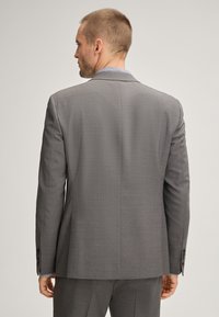 Gray tailored blazer with a textured weave, notched lapel, single vent, and buttoned cuffs. Worn over a light patterned shirt.