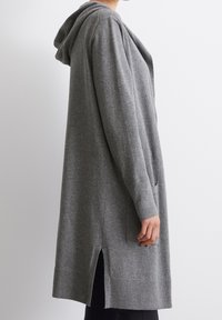 Grå lång kofta i mjukt material, med huva, sidofickor och slitsar, samt ribbade mudd och nederkant för ökad textur.