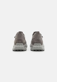 Zapatillas de ante gris con un acabado texturizado, que cuentan con una suela de goma gruesa y un diseño de tacón distintivo. Dos tiradores en la parte posterior.