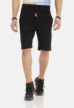 Shorts noirs en coton avec une taille élastique et un cordon de serrage orange, dotés de poches latérales et d'une coupe décontractée. Portés avec des baskets noires.