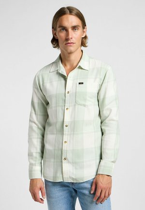 Grün-weißer kariert button-up Hemd aus weichem Stoff mit goldenen Knöpfen und einer Brusttasche; getragen mit hellblauen Jeans.