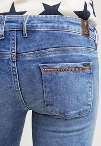 Jeans aus Denim in Hellblau mit einer figurnahe Passform. Verfügt über eine markante, mit Reißverschluss zu schließende Gesäßtasche und kontrastierende Nähte.