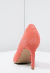 Korálové semišové lodičky na vysokém podpatku s špičatou špičkou a štíhlým stiletto podpatkem. Hladká textura a minimalistický design, žádné další akcenty.