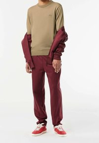 Sweter khaki o fakturze prążkowanej, zestawiony z bordowymi spodniami dresowymi z bocznymi pasami, uzupełniony czerwono-białymi sneakersami.