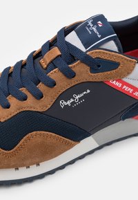 Bruna mocka- och marinblå mesh-sneakers med mörkblå snören, vita och grå accenter, samt en "Pepe Jeans London"-logga. Texturerad yta.