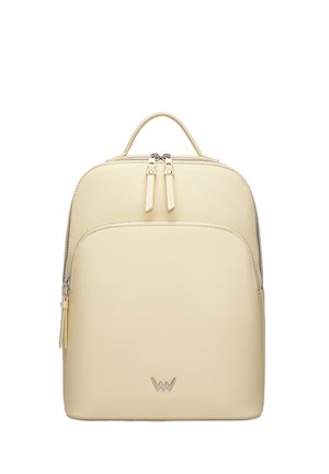 Beige rectangular backpack with two top zipper pulls, front zipper pocket, small handle, and minimalist metal logo on the front.