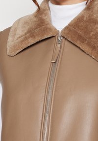 Brązowa skórzana kurtka z miękkim, jasnobrązowym futrzanym kołnierzem. Posiada srebrny zamek błyskawiczny z przodu. Gładka textura na całej powierzchni.