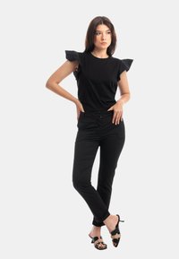 Top nero a maniche corte con spalline arricciate, abbinato a pantaloni neri aderenti e décolleté neri con open toe. Struttura liscia su tutta la superficie.