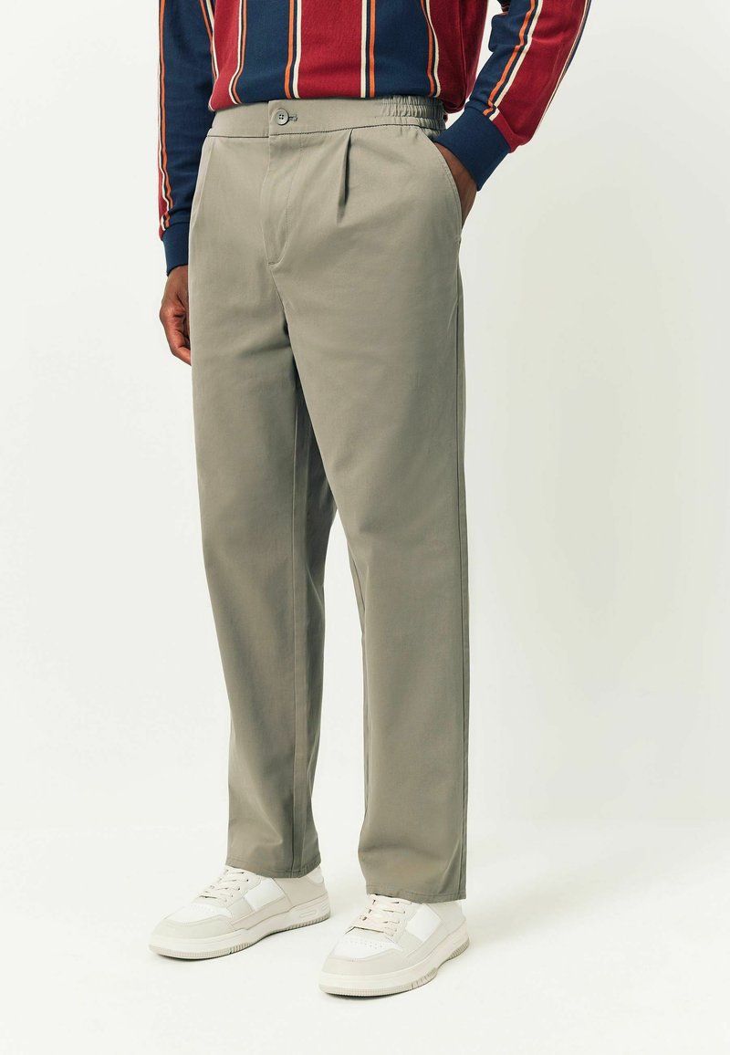 Light gray trousers with a smooth texture, featuring side pockets, a button closure, and subtle pleats at the front. Paired with white sneakers.