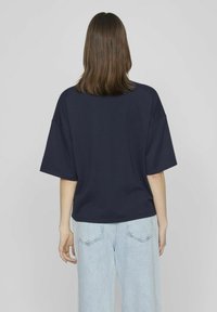 Camiseta de gran tamaño en azul marino con mangas cortas y escote redondo, combinada con jeans de tiro alto en azul claro. Diseño sencillo, tela suave.