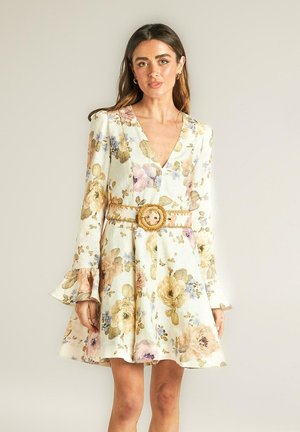 Vestido floral con mangas largas y acampanadas, presenta colores pasteles sobre un fondo claro, adornado con un cinturón trenzado y hebilla redonda.