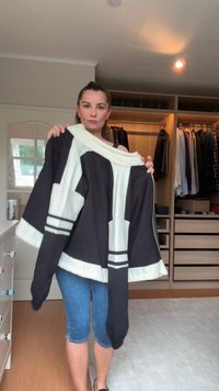 Chaqueta de gran tamaño en negro y crema con mangas anchas, que presenta rayas horizontales blancas cerca del dobladillo. Tejido suave con un diseño audaz.