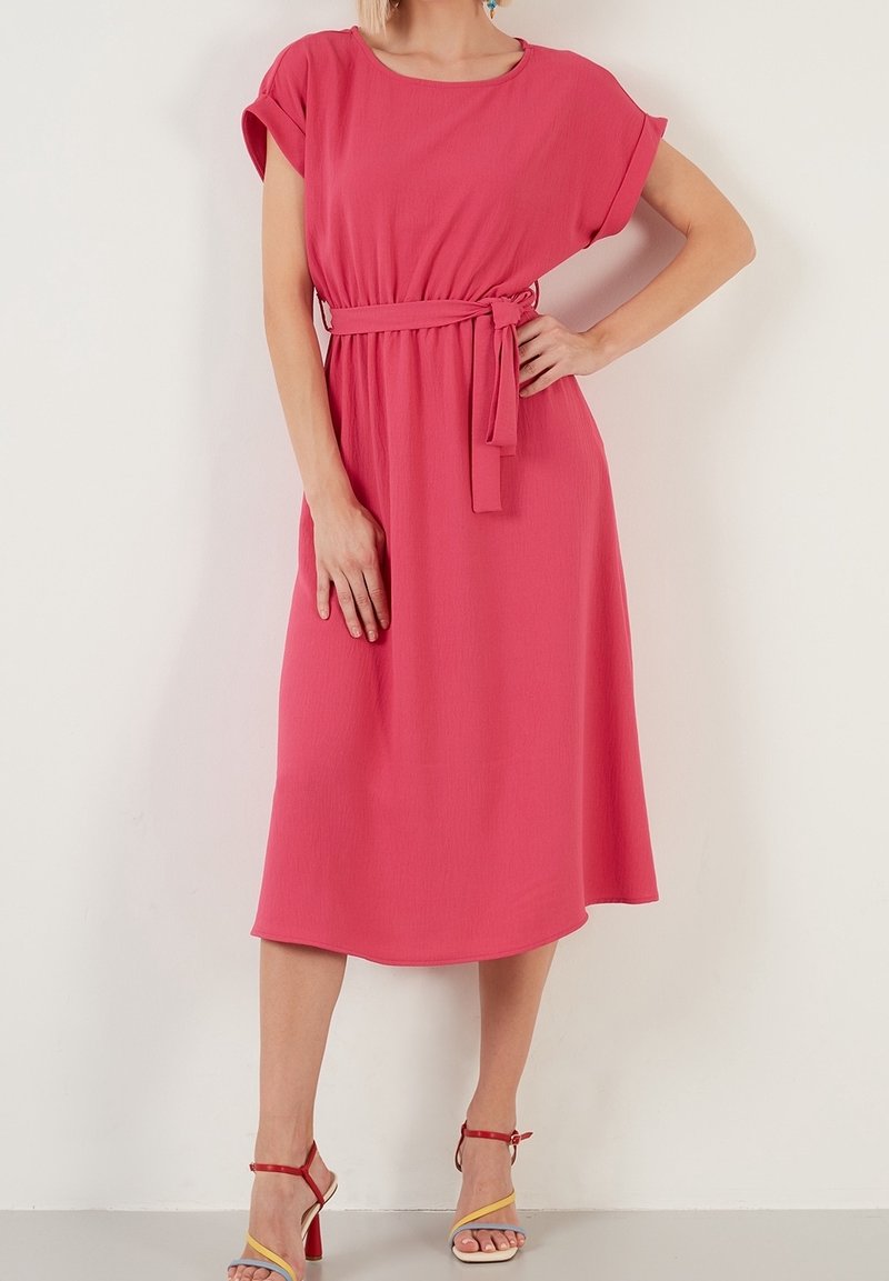 Rosa midi-klänning med korta ärmar och midjesnöre. Mjuk, strukturerad tyg; lätt utsvängd fåll. Kombinerad med flerfärgade klacksandaler.