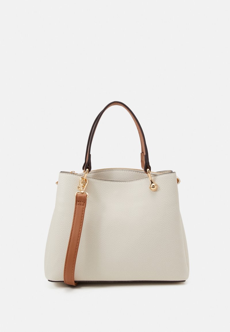 Sac à main beige clair texturé avec une bandoulière marron amovible, fermeture éclair et ferrures dorées. Caractérisé par une forme arrondie et deux poignées.